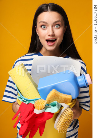 Surprised young woman with cleaning tools in hands on orange background Surprised young woman with cleaning tools in hands on orange background 116617284