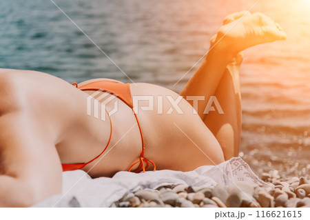 Happy young woman sunbathing or tanning on a seaside beach during summer vacation. smiling tourist in red swimsuit enjoying sun tan lying on beach near to calm clear sea water. 116621615