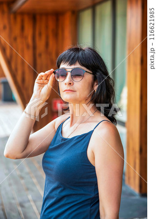 50 years old russian woman in short dress holding her sunglasses on the summer day 50 years old russian woman in short dress holding her sunglasses on the summer day 116621985