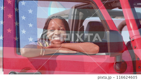 Image of flag of usa over happy african american woman in car by beach 116624605