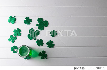 Image of glass with green beer, clover and copy space on white wooden background 116628053
