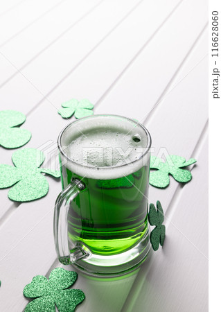 Image of glass with green beer, clover and copy space on white wooden background 116628060