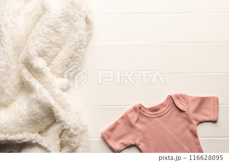 Cozy blanket and onesie on wood evoke newborn warmth and preparation. Cozy blanket and onesie on wood evoke newborn warmth and preparation. 116628095