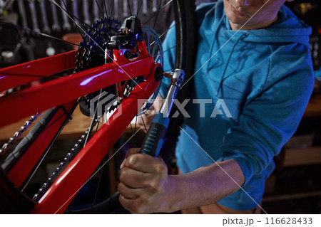 Busy hipster man bike mechanic removing rear wheel at garage workshop Busy hipster man bike mechanic removing rear wheel at garage workshop 116628433
