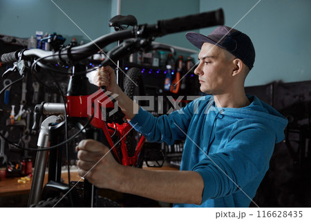 Handsome young man mechanic repairing bike working at bicycle workshop 116628435
