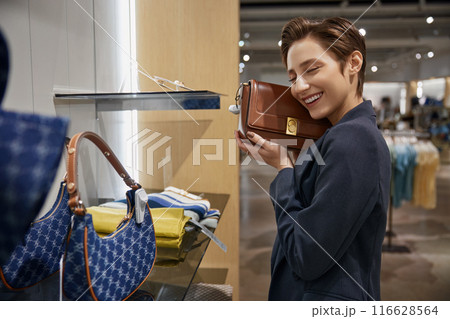 Young elegant woman buyer selecting designer leather handbag in store 116628564
