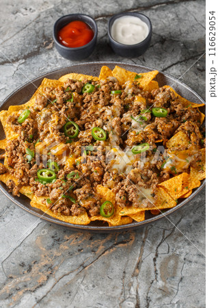 Loaded Beef and Cheese Nachos with jalapeno peppers and sauces closeup on the plate. Vertical 116629054