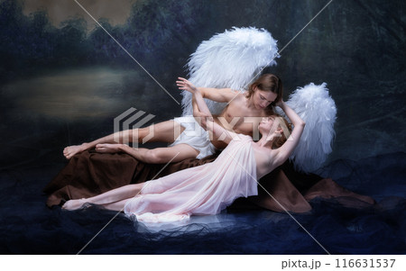 Young man with angelic wings tenderly embracing elegant young woman in white attire against vintage green background. 116631537