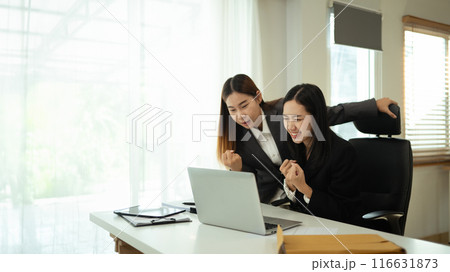Happy excited business women looking at laptop celebrating business success at office 116631873