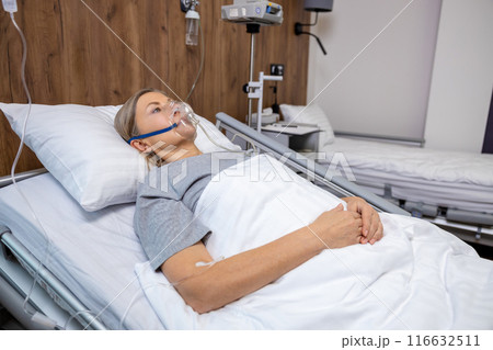 Blonde mid aged woman lying in bed in hospital with an oxygen mask on her face 116632511