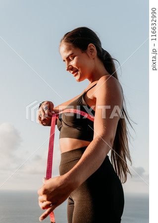 A woman is holding a pink tape measure and is measuring her chest after morning fitness 116632990