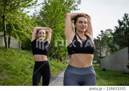 Woman with overweight warming up and exercising for dieting and health with her trainer in park Woman with overweight warming up and exercising for dieting and health with her trainer in park 116633201