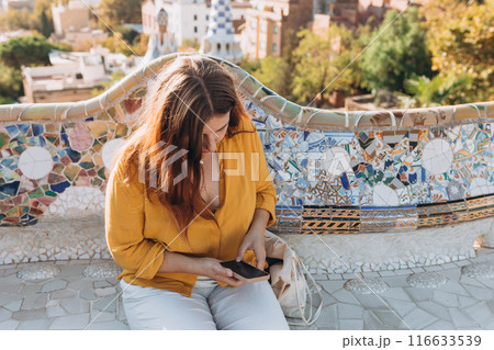 Beautiful female in Gaudi garden, Spain, Barcelona. Young traveling using smart phone outdoors. Concept of travel, tourism and vacation in city. Park Guell 116633539