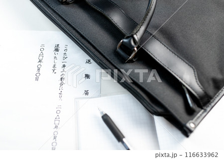 ビジネスバッグの傍らに置かれた手書きの退職届とメモ帳の上に置かれたゲルインクの黒いペン 116633962