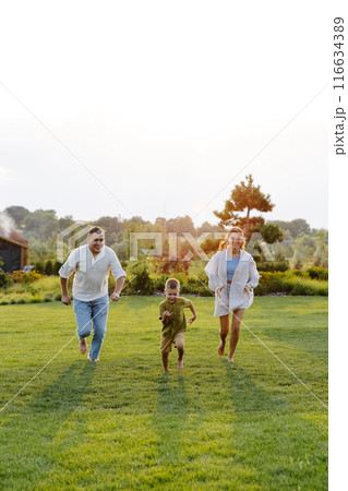 A Family Joyfully Running Across a Lush Green Grass Field on a Warm Summer Day, Basking in the Sunshine and Laughter A Family Joyfully Running Across a Lush Green Grass Field on a Warm Summer Day, Basking in the Sunshine and Laughter 116634389