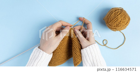 Female hands knitting with yellow wool, blue background. Top view 116634571