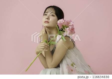 ピンク背景の花を持つ若い女性のポートレート 116634830