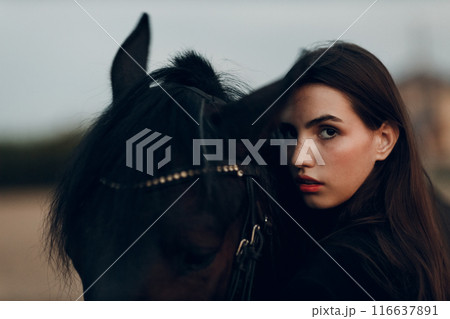 Young woman in black with her horse at sunset outdoors 116637891