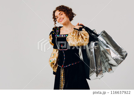 Young adult smiling woman dressed in a medieval dress holding shopping bags in hands isolated white background 116637922