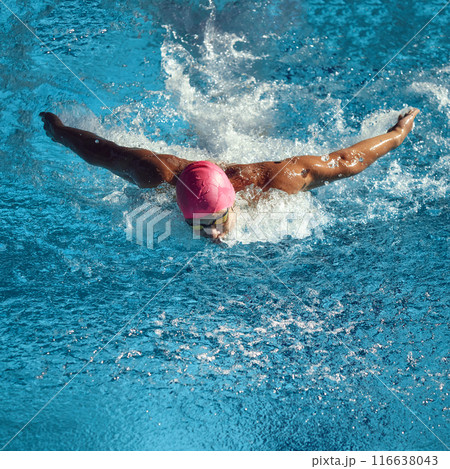 Athlete in pink swim cap and goggles executes butterfly stroke in pool, capturing intensity and movement of competitive swimming in action. 116638043