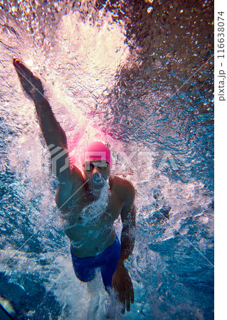 Underwater shot. Male swimmer mid-stroke, showcasing his strength and precision, with blue swimwear and goggles, swimming in pool. Underwater shot. Male swimmer mid-stroke, showcasing his strength and precision, with blue swimwear and goggles, swimming in pool. 116638074