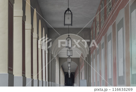 Long corridor with Antique lantern hanging from ceiling and Beautiful columns inside Hofgartenarkaden. Long corridor with Antique lantern hanging from ceiling and Beautiful columns inside Hofgartenarkaden. 116638269