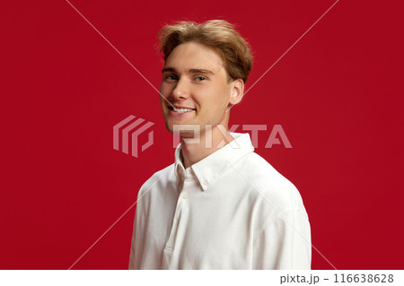 Portrait of handsome smiling young man, student, employee in white polo shirt, smiling, looking at camera against red studio background. Portrait of handsome smiling young man, student, employee in white polo shirt, smiling, looking at camera against red studio background. 116638628