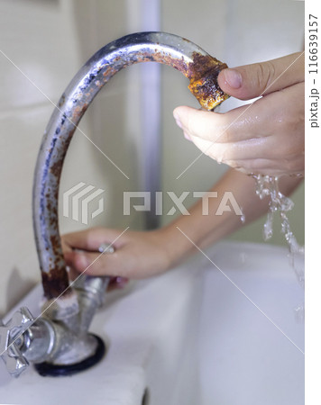 A child washes his hands with water from a rusty tap. Old plumbing, damage and fungus, rust. Unsanitary conditions in the bathroom 116639157