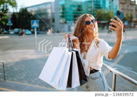 Beautiful woman with shopping bags makes selfie. Young woman walking shopping. Lifestyle concept. Beautiful woman with shopping bags makes selfie. Young woman walking shopping. Lifestyle concept. 116639572