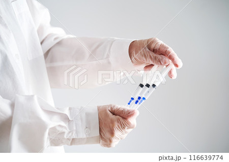 The doctor's hands in a white coat and gloves hold three syringes with medicine. 116639774