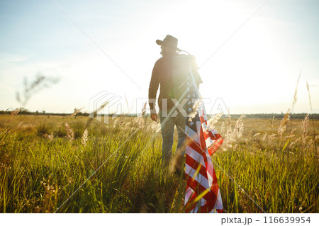 4th of July. American Flag. Traveler with the flag of America. The man in a hat, a backpack, a shirt and jeans. 4th of July. American Flag. Traveler with the flag of America. The man in a hat, a backpack, a shirt and jeans. 116639954