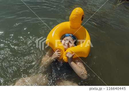 A portrait of a nine-year-old girl with a funny face inside a yellow inflatable duck float. She is smiling and enjoying her summer vacation while floating in the lake 116640445