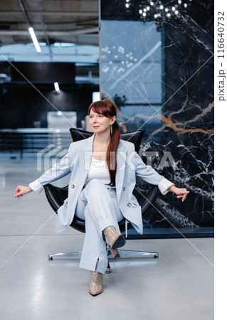 Woman in light blue suit posing in a modern office space 116640732