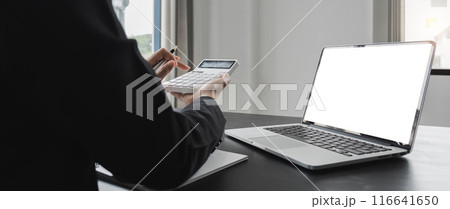 Close up Business woman using calculator and laptop for do math finance on wooden desk in office and business working background, tax, accounting, statistics and analytic research concept 116641650