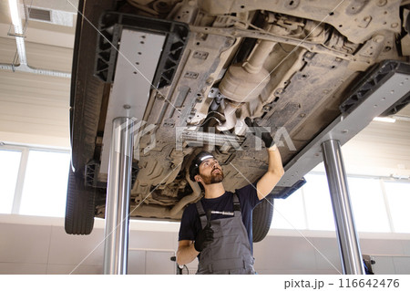 Mechanic inspecting car undercarriage at auto repair shop 116642476