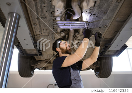 Mechanic working underneath car on lift in auto repair shop Mechanic working underneath car on lift in auto repair shop 116642523