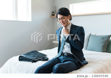 ベッドに座る疲れたスーツ姿の若いビジネスマン(飲み過ぎ・二日酔い・朝帰り・酔っ払い) ベッドに座る疲れたスーツ姿の若いビジネスマン(飲み過ぎ・二日酔い・朝帰り・酔っ払い) 116643540