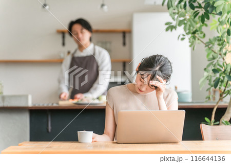 自宅でテレワークする女性・妻と心配そうに見つめる男性・夫 自宅でテレワークする女性・妻と心配そうに見つめる男性・夫 116644136