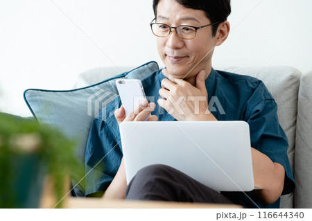 ソファでパソコンとスマホを操作するミドル男性 116644340