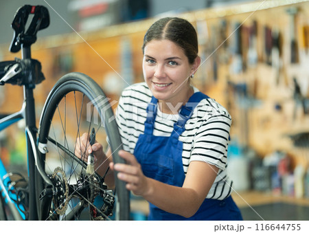 Smiling female mechanic adjusting bicycle wheel in repair shop Smiling female mechanic adjusting bicycle wheel in repair shop 116644755