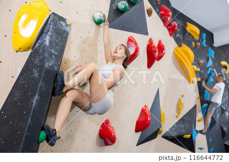 Young woman climbs steep artificial wall in sports complex and trains endurance 116644772
