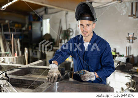 During manufacture of product, man employee works with welding machine 116644870