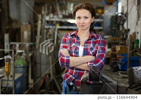 Female employee of workshop stands next to vise, resting from labors Female employee of workshop stands next to vise, resting from labors 116644904