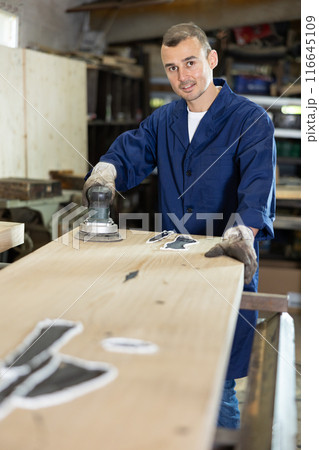 During manufacturing, man employee grinds surface of wooden board, gives smoothness to surface During manufacturing, man employee grinds surface of wooden board, gives smoothness to surface 116645109