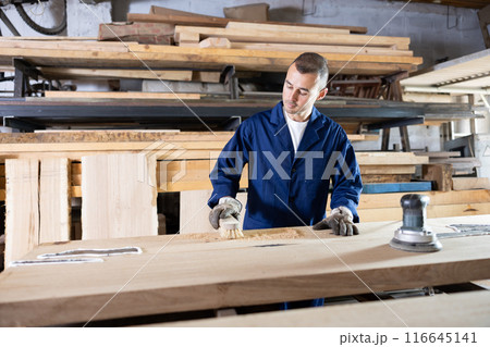 Male sawmill worker cleaning up excess resin or glue on wooden board 116645141