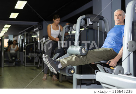 Elderly man trains his legs on machine 116645239