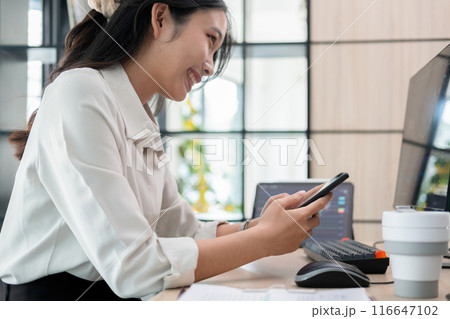 Woman examines stock graphs at office desk using phone 116647102