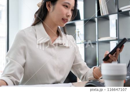 Woman examines stock graphs at office desk using phone 116647107