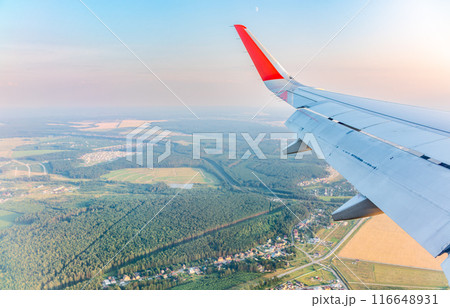 View of airplane wing, blue skies and green land during landing. Airplane window view. 116648931