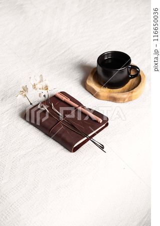 Notebook and coffee cup on the white blanket. 116650036